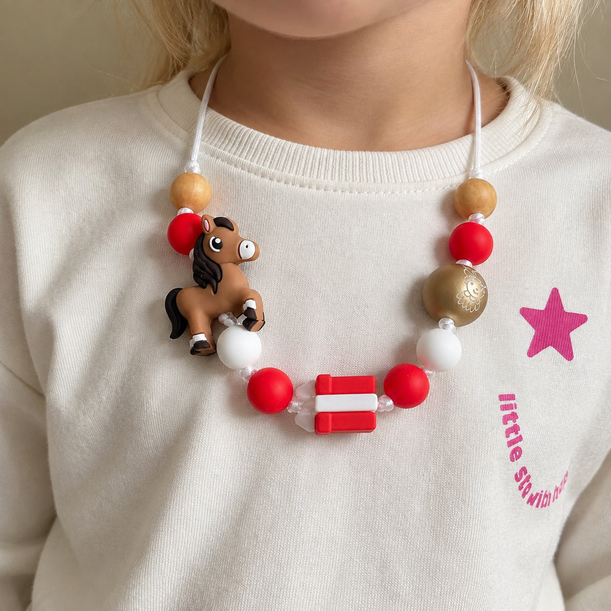 Meisje draagt peuterketting met rode, witte en gouden kralen en een paardje